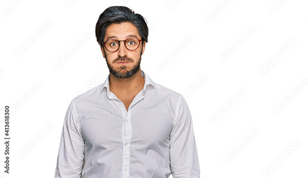 Young hispanic man wearing business shirt and glasses puffing cheeks with funny face. mouth inflated with air, crazy expression. Young hispanic man wearing business shirt and glasses puffing cheeks with funny face. mouth inflated with air, crazy expression.