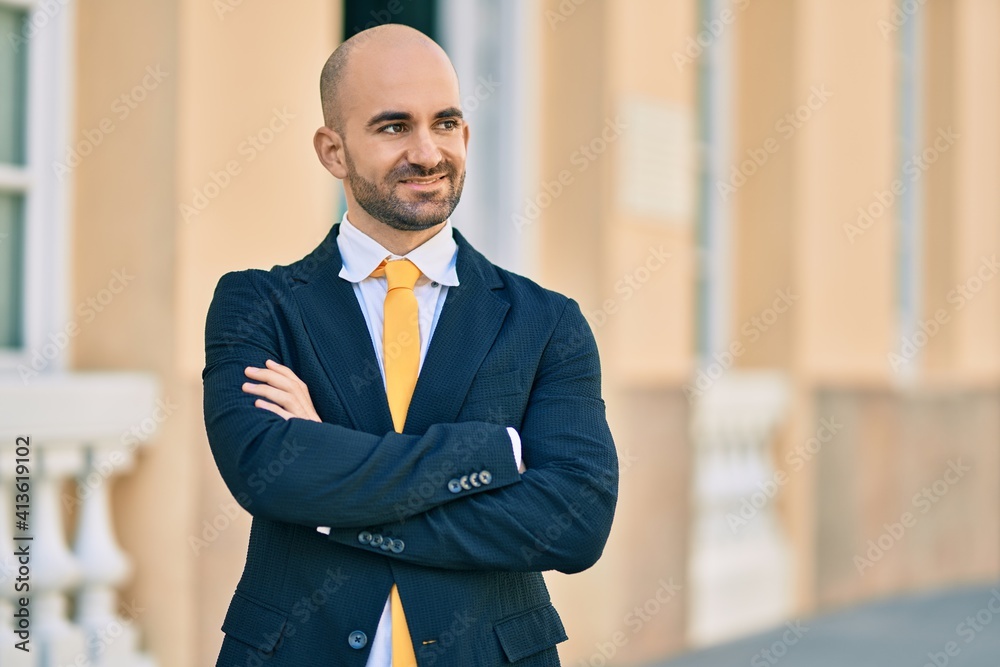 Fototapeta premium Young hispanic bald businessman with arms crossed smiling happy at the city.