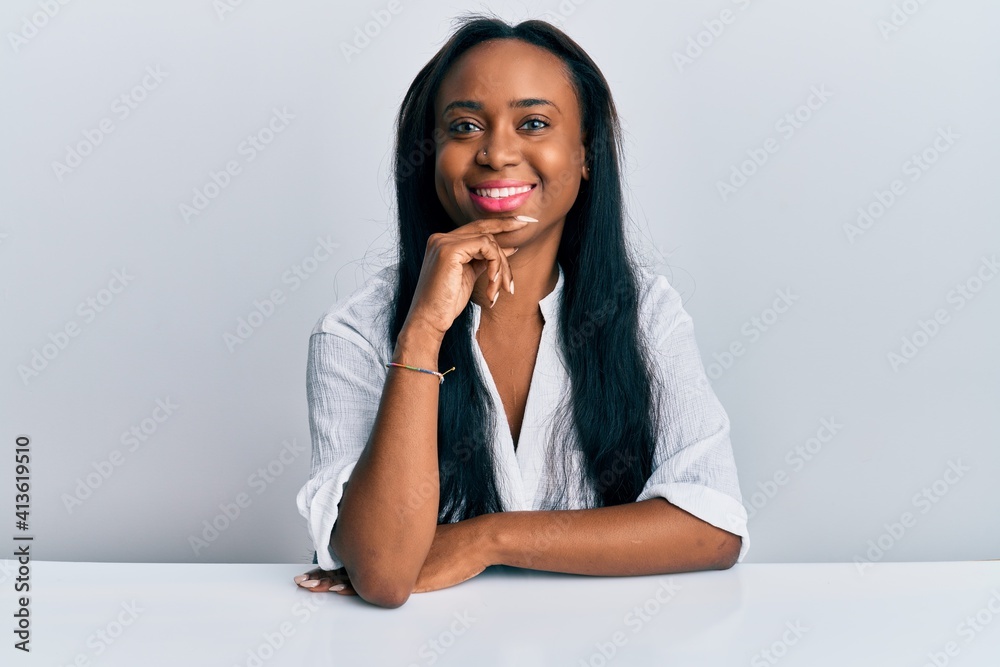 Young african woman wearing casual clothes sitting on the table smiling looking confident at the camera with crossed arms and hand on chin. thinking positive. Young african woman wearing casual clothes sitting on the table smiling looking confident at the camera with crossed arms and hand on chin. thinking positive.