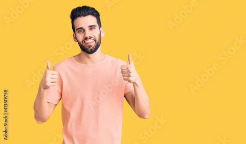 Young handsome man with beard wearing casual t-shirt success sign doing positive gesture with hand, thumbs up smiling and happy. cheerful expression and winner gesture.
