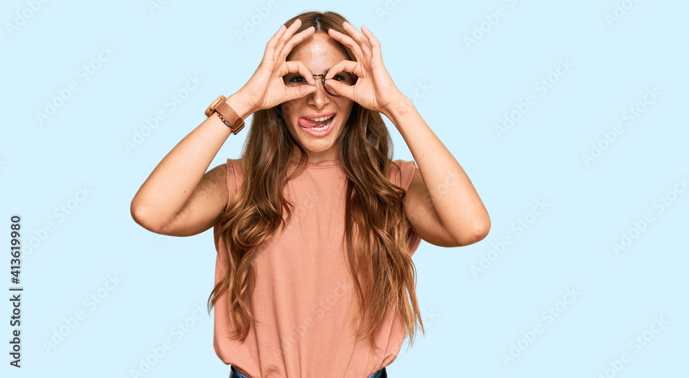 Young hispanic woman wearing casual clothes and glasses doing ok gesture like binoculars sticking tongue out, eyes looking through fingers. crazy expression. Young hispanic woman wearing casual clothes and glasses doing ok gesture like binoculars sticking tongue out, eyes looking through fingers. crazy expression.