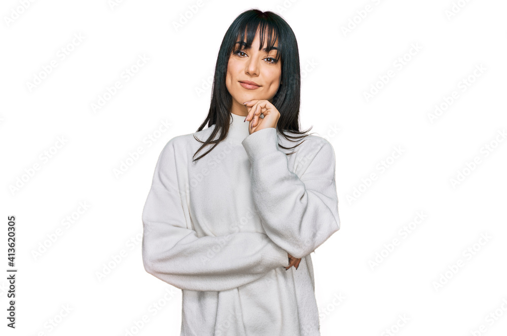 Young brunette woman with bangs wearing casual turtleneck sweater looking confident at the camera with smile with crossed arms and hand raised on chin. thinking positive. Young brunette woman with bangs wearing casual turtleneck sweater looking confident at the camera with smile with crossed arms and hand raised on chin. thinking positive.