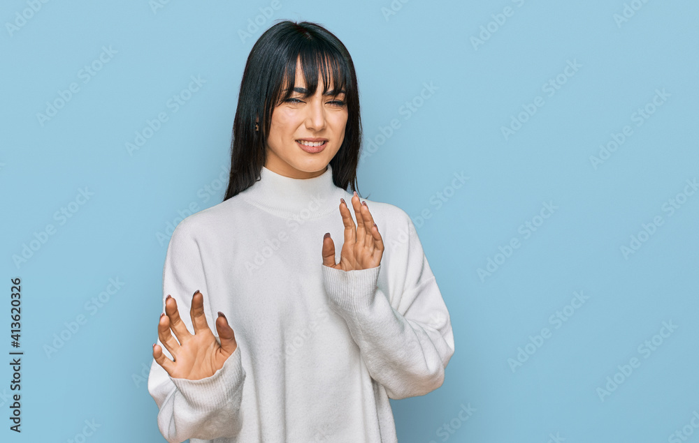 Young brunette woman with bangs wearing casual turtleneck sweater disgusted expression, displeased and fearful doing disgust face because aversion reaction. with hands raised Young brunette woman with bangs wearing casual turtleneck sweater disgusted expression, displeased and fearful doing disgust face because aversion reaction. with hands raised