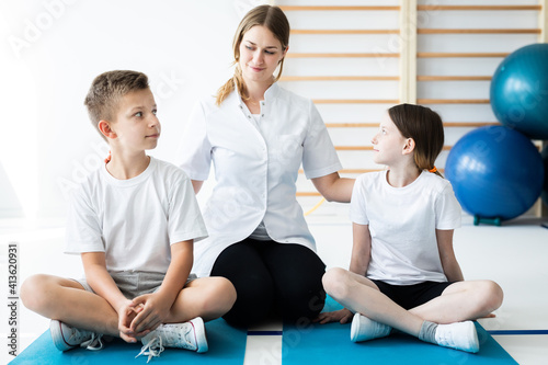 Two kids sitting on blue mats with their professional physical education trainer