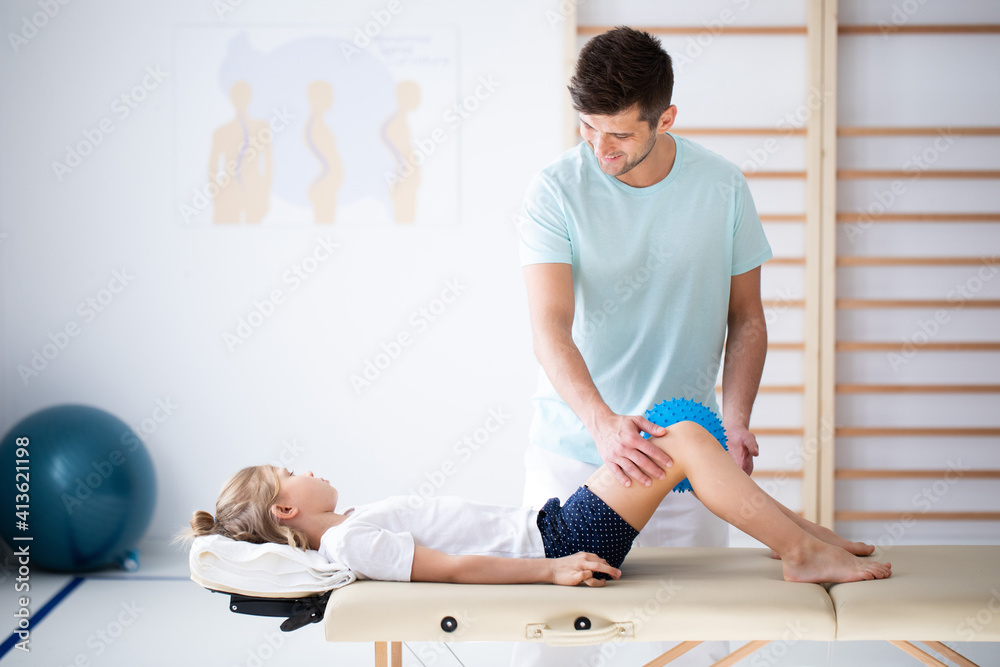 Cute little injure girl on massage table exercising with young male doctor Cute little injure girl on massage table exercising with young male doctor