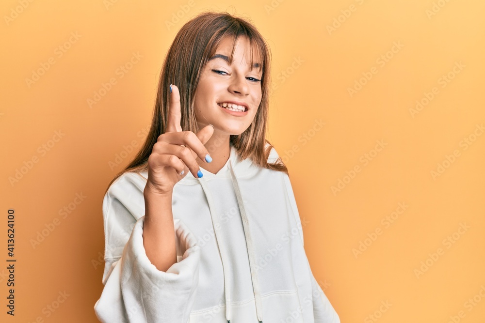 Teenager caucasian girl wearing casual sweatshirt smiling with an idea or question pointing finger up with happy face, number one Teenager caucasian girl wearing casual sweatshirt smiling with an idea or question pointing finger up with happy face, number one