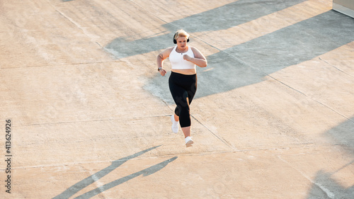 High angle view of plus size woman running outdoors. Young curvy female in sportswear jogging on roof.