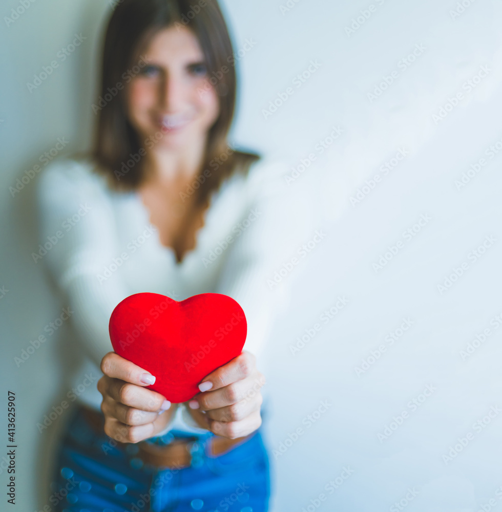 Blond blonde girl holding a red heart in the foreground. The background is white and the image has selective blur. Blond blonde girl holding a red heart in the foreground. The background is white and the image has selective blur.
