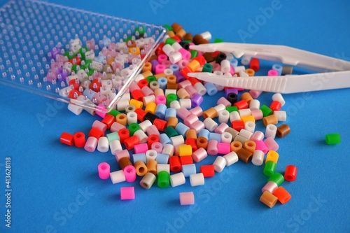 colorful ironable beads, template and tweezers on light blue background photo