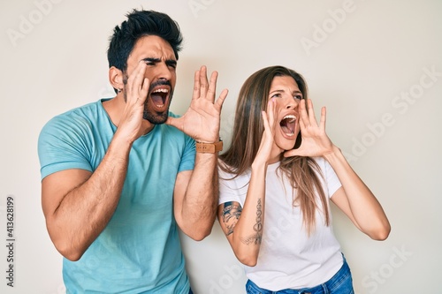 Beautiful young couple of boyfriend and girlfriend together shouting angry out loud with hands over mouth