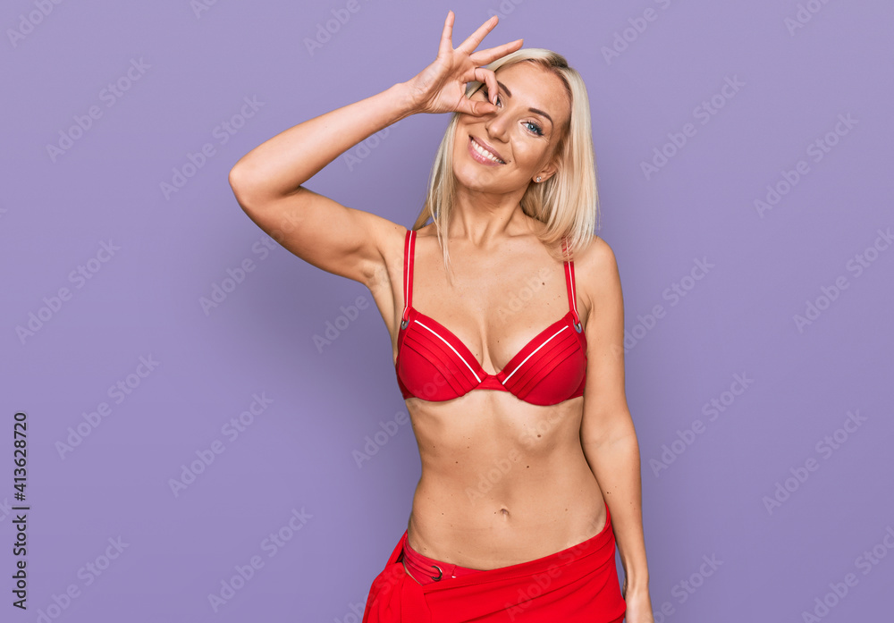 Naklejka premium Young blonde woman wearing bikini smiling happy doing ok sign with hand on eye looking through fingers