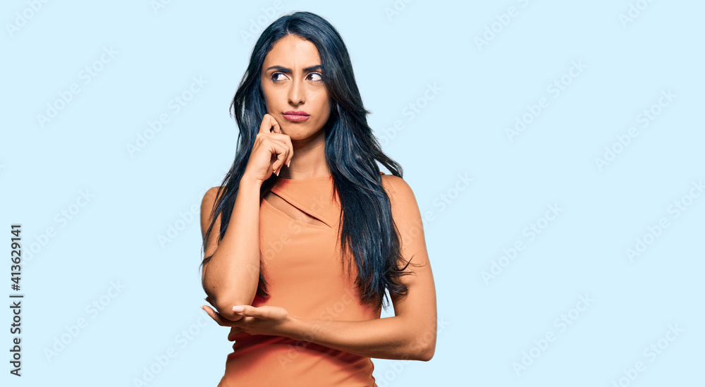 Fototapeta premium Beautiful hispanic woman wearing summer dress serious face thinking about question with hand on chin, thoughtful about confusing idea