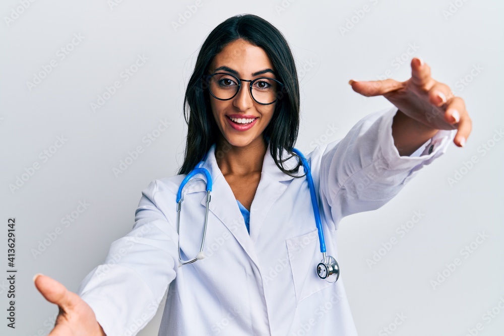 Beautiful hispanic woman wearing doctor uniform and stethoscope looking at the camera smiling with open arms for hug. cheerful expression embracing happiness. Beautiful hispanic woman wearing doctor uniform and stethoscope looking at the camera smiling with open arms for hug. cheerful expression embracing happiness.