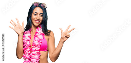 Beautiful hispanic woman wearing bikini and hawaiian lei showing and pointing up with fingers number eight while smiling confident and happy.