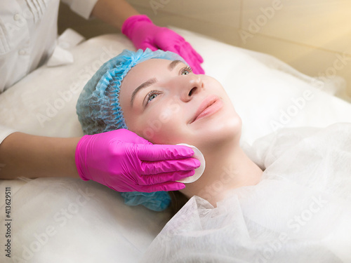 Face Skin Care. Professional cosmetologist is doing procedure of cleansing skin with pads. Hands of beautician and beautiful caucasian woman close up. Facial skincare. Beauty salon, cosmetology clinic