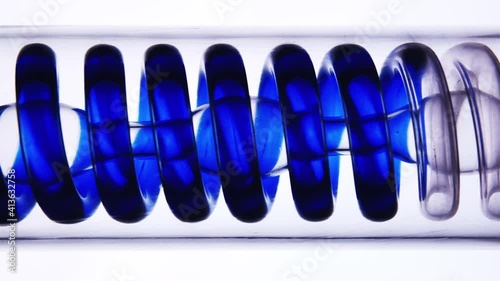 Blue liquid flows through a spiral glass laboratory test tube. Flask with a spiral inside. Filtration of liquidity. Production of perfumery and cosmetics.