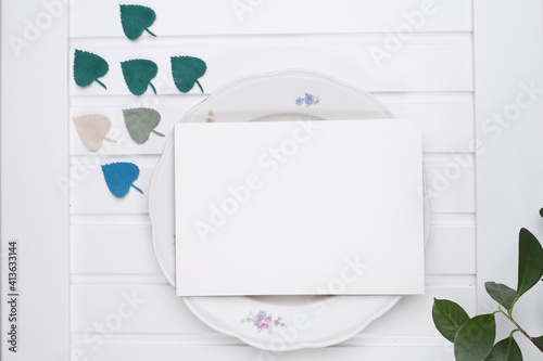 Kartka papieru na porcelanowym talerzu i listki na białym stole