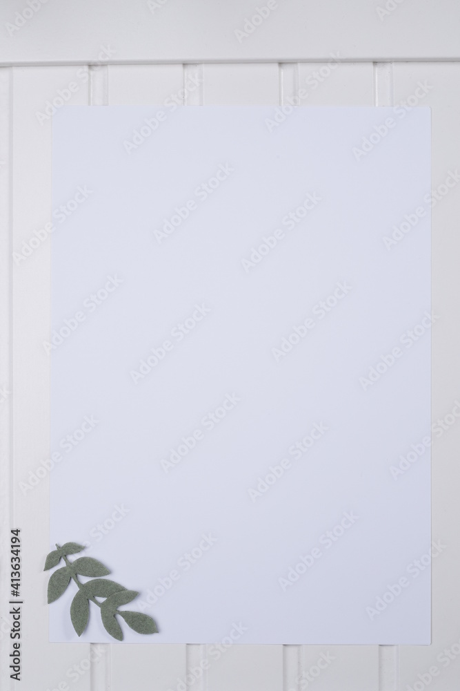 Kartka papieru biała na białym blacie drewnianym z listkami zielonymi - obrazy, fototapety, plakaty 