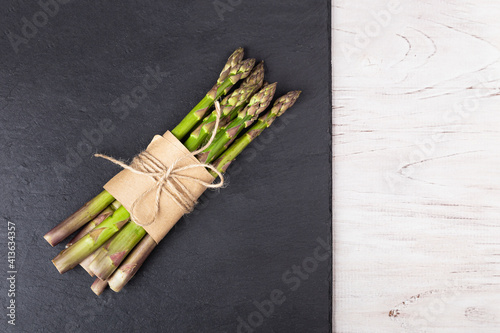 Green asparagus wrapped in paper and tied with a rope on a slate dish on a white wooden background. Healthy eating concept
