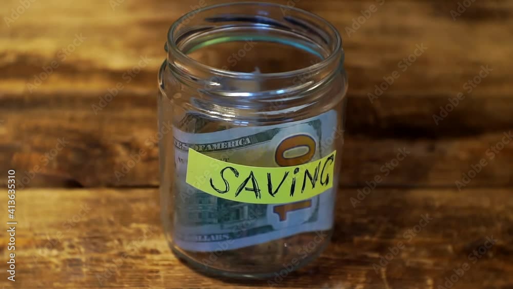 saving money.hand puts a few hundred dollar bills in a savings jar.close-up saving money.hand puts a few hundred dollar bills in a savings jar.close-up