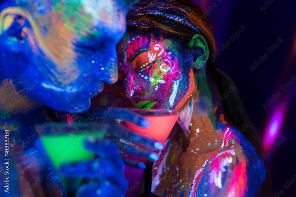 Young couple drink an alcoholic drink in a nightclub. Man and woman with fluorescent bodyart