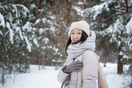 Portrait of a positive fashionable Korean young woman on a walk in a winter snowy cold forest.