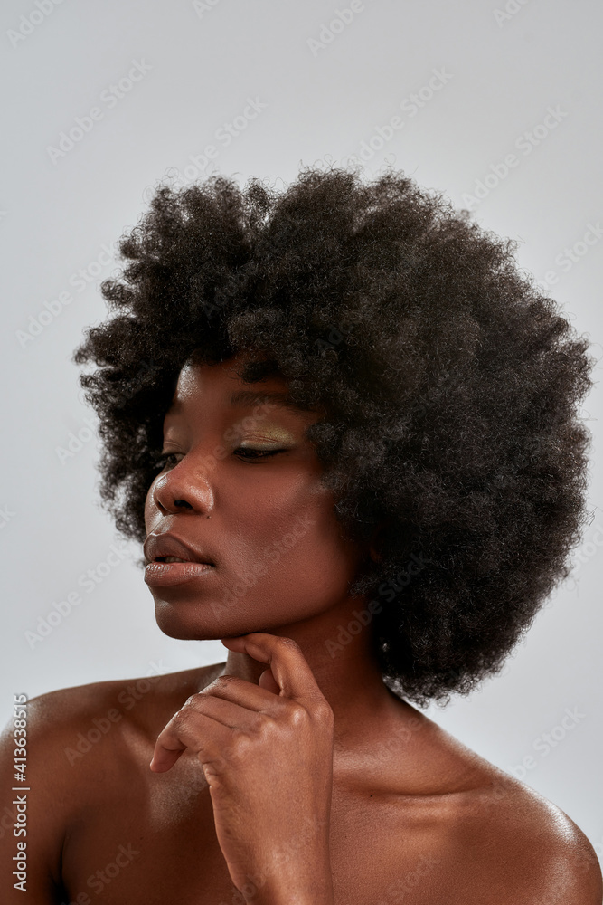 Portrait of beautiful african american woman with afro hair and perfect glowing skin looking aside, posing isolated over gray background