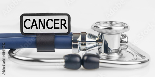On the white surface lies a stethoscope with a plate with the inscription - CANCER