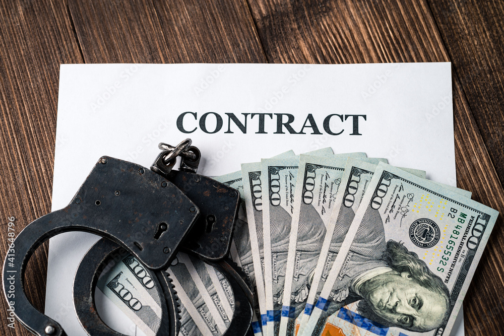 concept handcuffs and dollars are on the contract, American dollar bills on a wooden background concept handcuffs and dollars are on the contract, American dollar bills on a wooden background