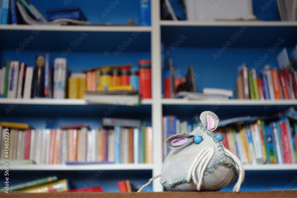 Slebstgebastelte Stoffspielzeug Maus vor buntem chaotischen Bücherregal. Lesemaus mit blauen Augen, Schnurrbarthaaren und treuem Hundeblick. Slebstgebastelte Stoffspielzeug Maus vor buntem chaotischen Bücherregal. Lesemaus mit blauen Augen, Schnurrbarthaaren und treuem Hundeblick.