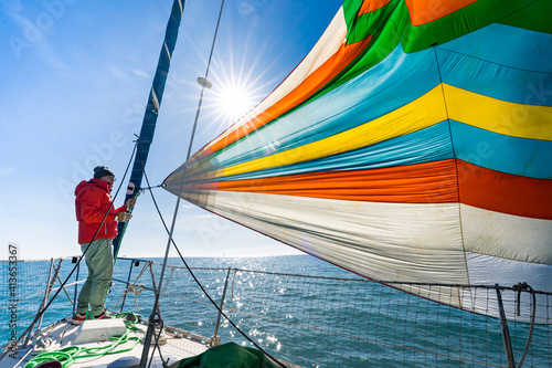 Foto Un homme en veste rouge au devant d'un voilier avec une voile multicolore