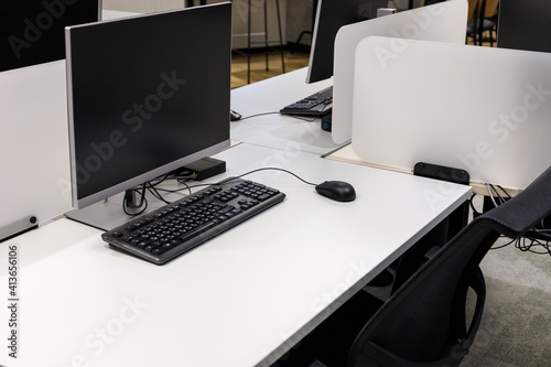 Computer monitor on an empty desk in a modern office with black keyboard and wired mouse