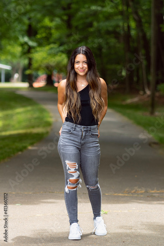 Portrait of a beautiful smiling young woman in park modeling jeans