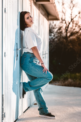 chica joven morena con pantalones vaqueros azules y camiseta blanca apilada sobre puertas de madera blancas en el campo