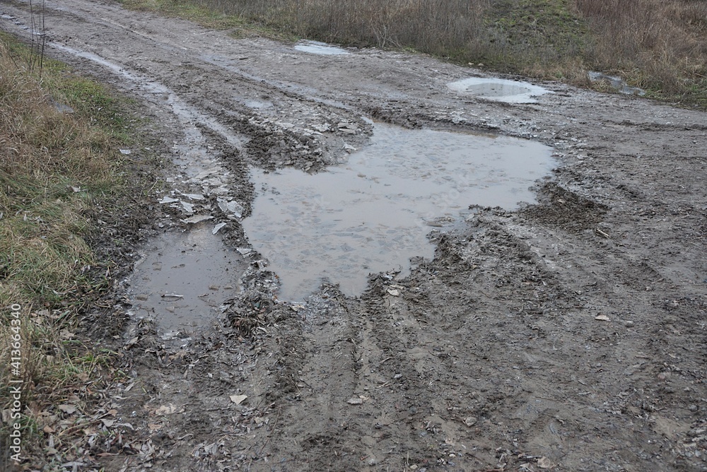 part of a rural road of gray earth with a large pothole and frozen muddy water in the ice part of a rural road of gray earth with a large pothole and frozen muddy water in the ice