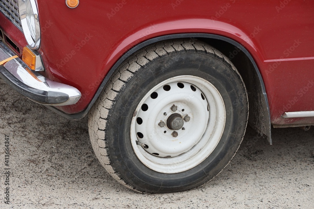 one black white old wheel on a red retro car stands on gray sand in the street