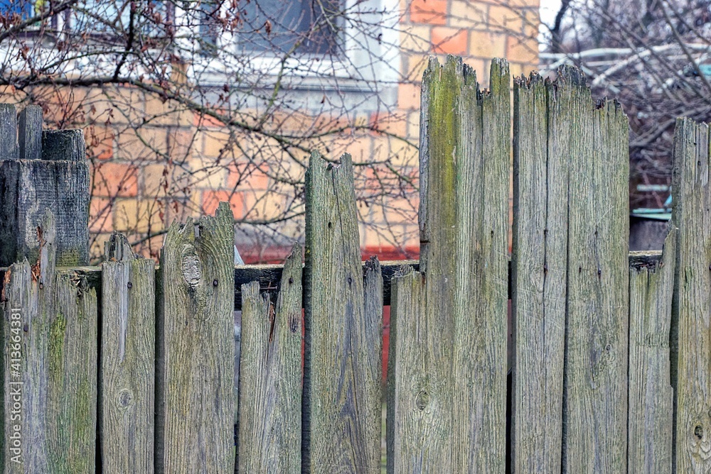 part of an old wooden gray green fence with broken boards on a rural street