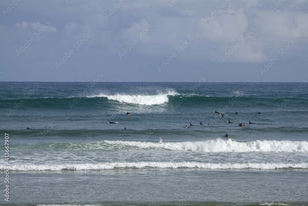 Many surfers sit and lie on their surfboards between breaking approaching waves on a beach in Portugal on the Atlantic Ocean