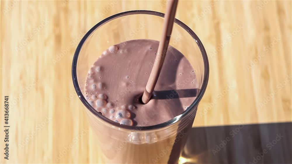 Slow motion clip of thick chocolate milk pouring into a clear drinking glass, viewed from above
