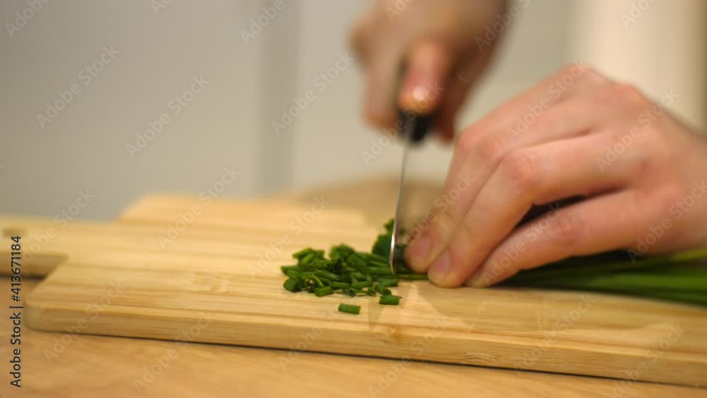 Close up of chives being chopped on wooden board by young woman in kitchen Close up of chives being chopped on wooden board by young woman in kitchen