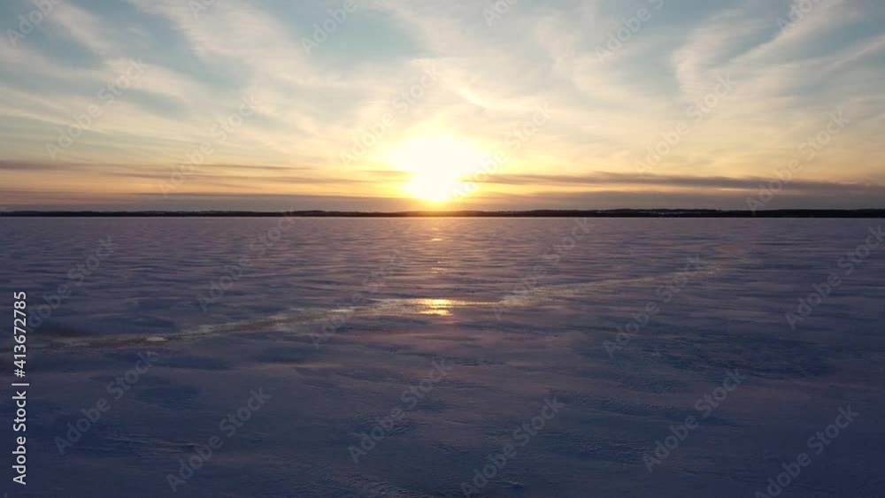 Flying low toward sunset over vast snow covered frozen lake with during winter; aerial Flying low toward sunset over vast snow covered frozen lake with during winter; aerial