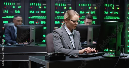 Smart female IT worker with glasses sitting in server room behind workplace, working with database on computer. System software concept. photo