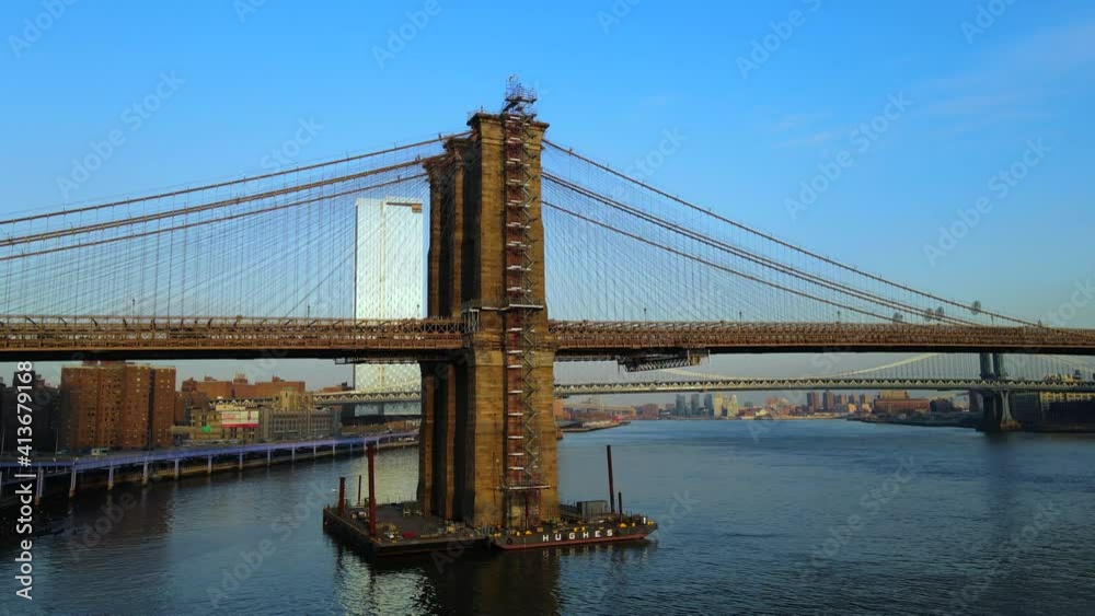 Aerial close view of stunning Brooklyn Bridge and Manhattan above East River flying backwards on sunny summer day in New York City, USA. Aerial close view of stunning Brooklyn Bridge and Manhattan above East River flying backwards on sunny summer day in New York City, USA.
