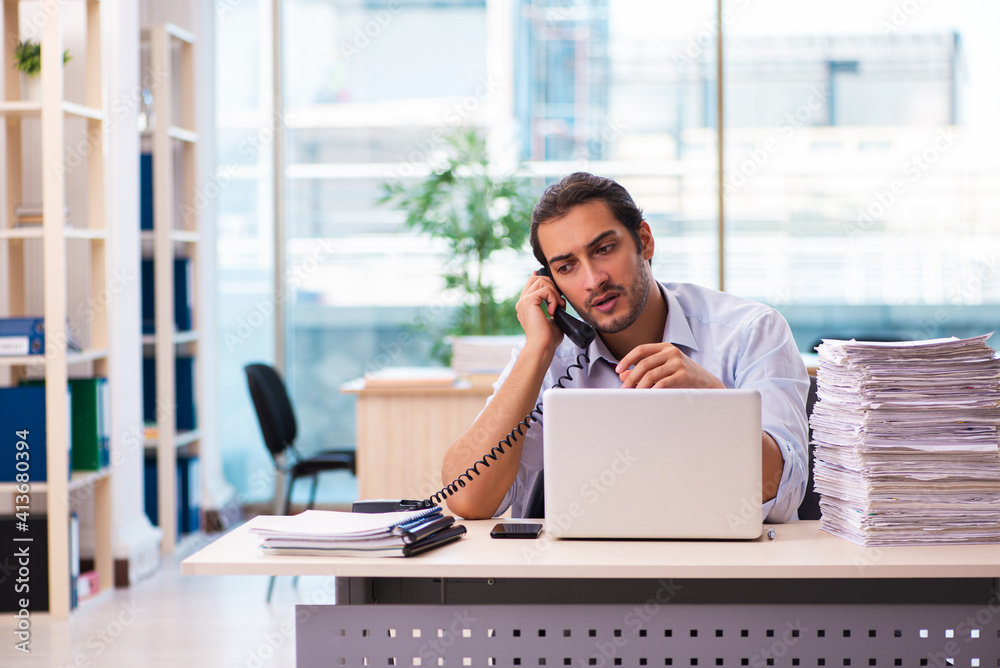 Young male employee unhappy with excessive work in the office Young male employee unhappy with excessive work in the office