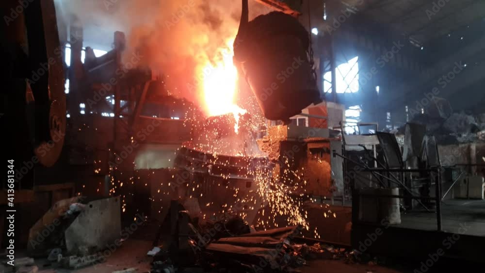 Hot liquid molten metal being poured from ladle into casting flask at steel fabrication industry. Slow motion.