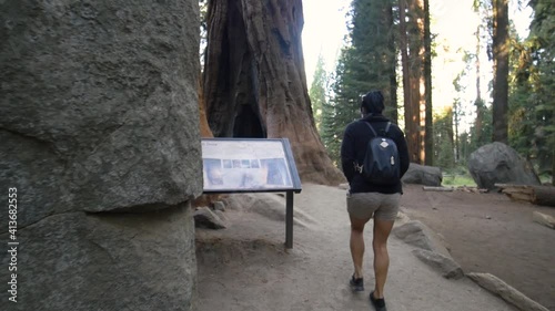 brunette woman walking along dirt path next to a large rock
