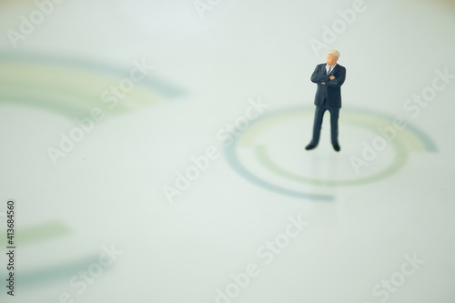 Miniature businessman in suit standing on center of circle.