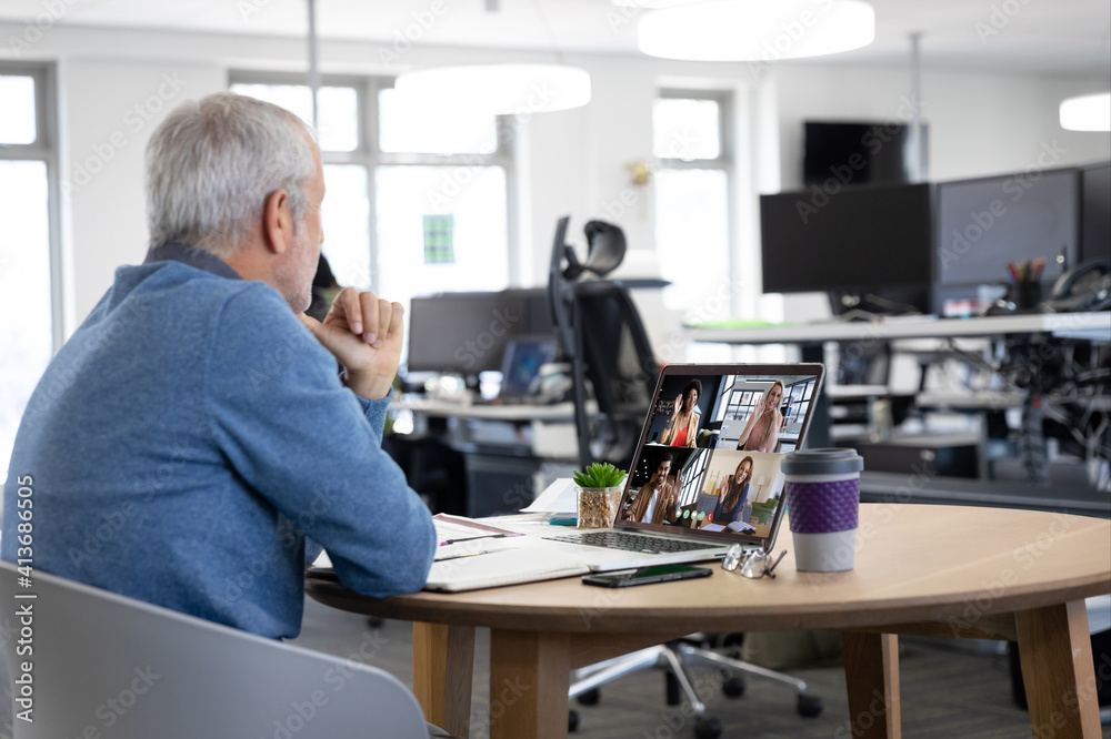 Caucasian man in office having video call with colleagues displayed on laptop screen