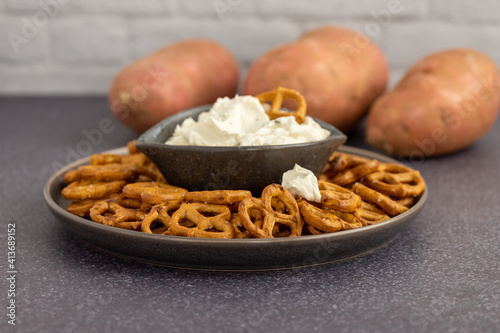 Healthy sweet potato pretzels in a tray with chive and onion cream cheese dip on a dark table and a white background. 