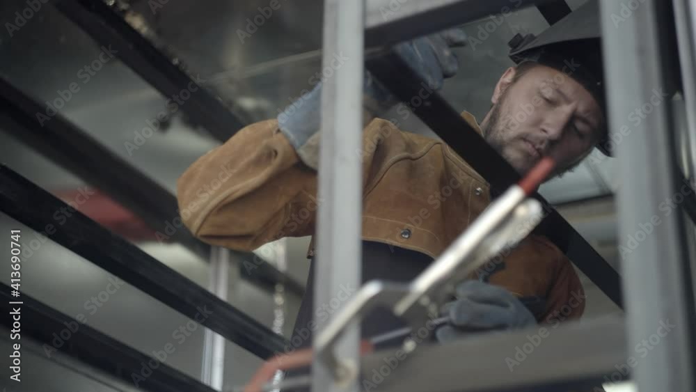 Welder takes off protective mask to check his work on metal frame Welder takes off protective mask to check his work on metal frame